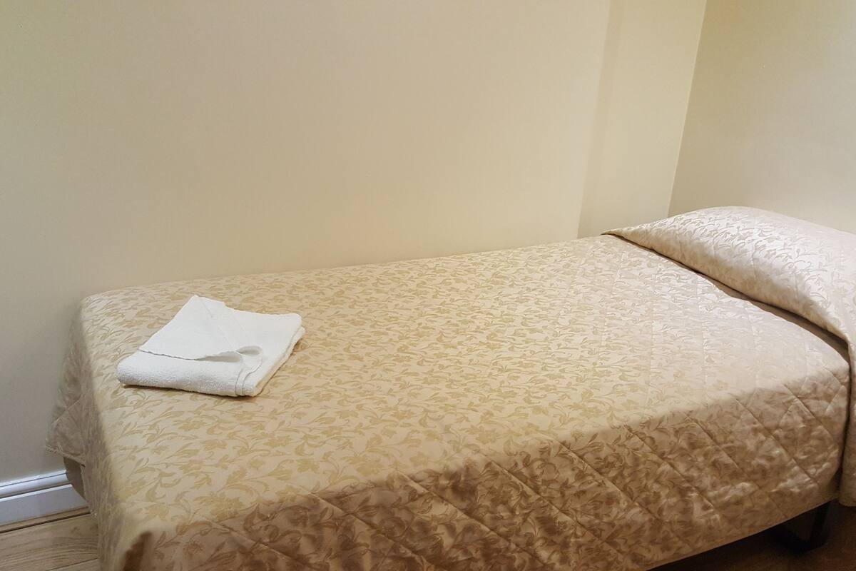 A small, single-bed room with a patterned bedspread and a neatly folded white towel on the bed.