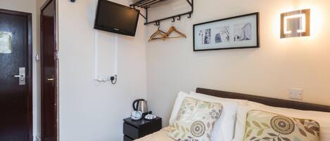 Quarto de hotel com cama, televisão fixada na parede, aquecedor, mesa pequena com chaleira e toalheiro na parede.
