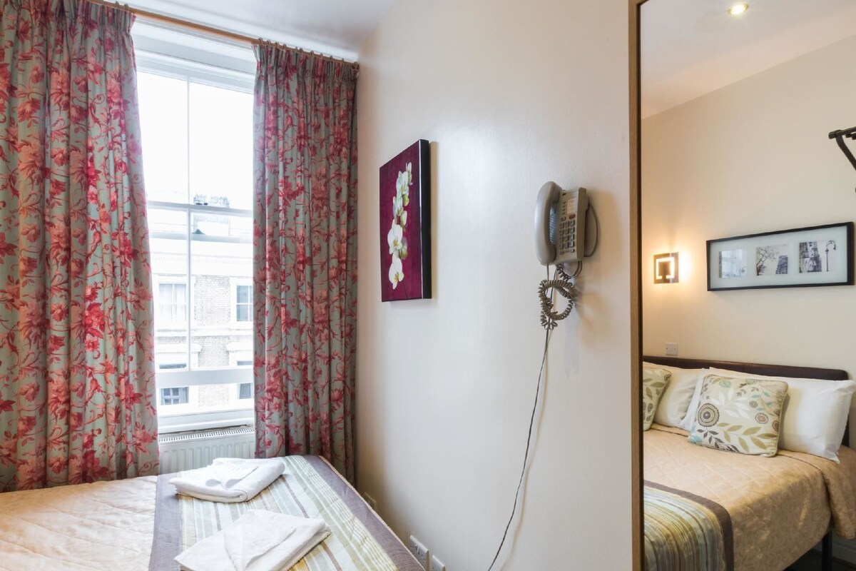 A hotel room with two beds, a telephone, a framed picture, and a window with curtains.