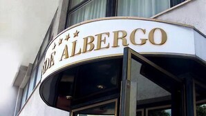 The exterior of a hotel named "Hotel Albergo" with a curved entrance and large windows.