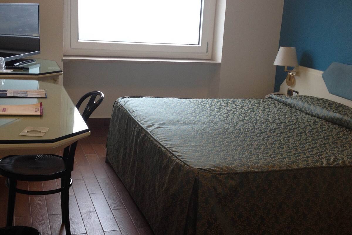 A small, simple room with a bed, a desk, and a chair.