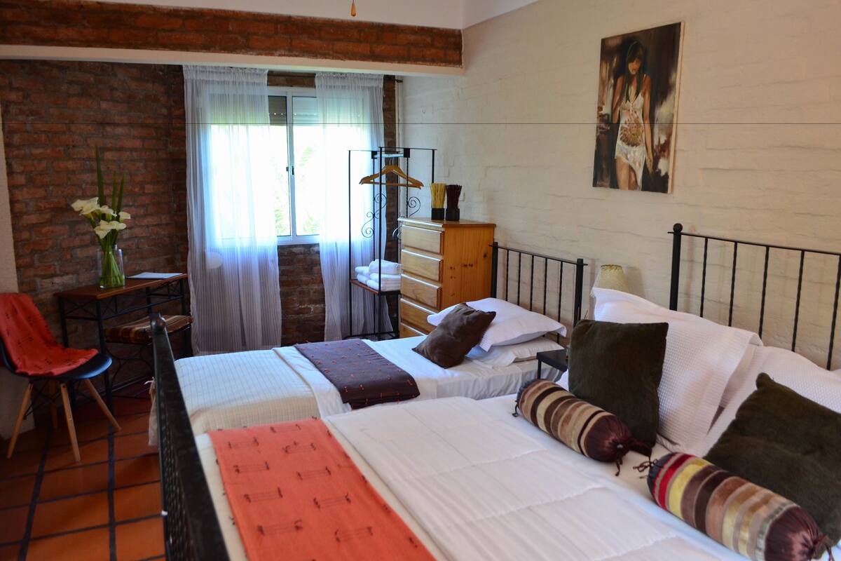 A bedroom with two beds, a wooden dresser, a chair, a hanging coat rack, and a painting on the wall.