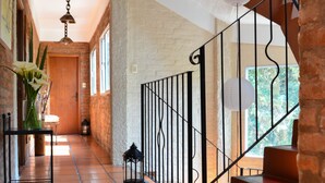 A hallway with a tiled floor, a staircase with a metal railing, and a door at the end. - Posada del Bosque (Colonia del Sacramento)