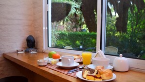 A breakfast table with a variety of food items and a window view of greenery. - Posada del Bosque (Colonia del Sacramento)