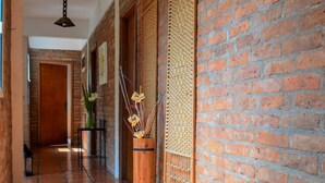 A hallway with a brick wall, a wooden bench, and a tiled floor. - Posada del Bosque (Colonia del Sacramento)
