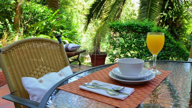 A dining table set with a white bowl, a glass of orange juice, and cutlery on a woven placemat. - Posada del Bosque (Colonia del Sacramento)