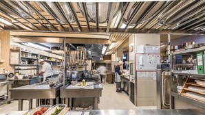 Une cuisine professionnelle dotée de surfaces en acier inoxydable, de plusieurs postes de cuisson et où des chefs préparent les plats.