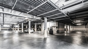 Un vaste garage souterrain avec des piliers en béton, des poutres métalliques et quelques voitures garées.