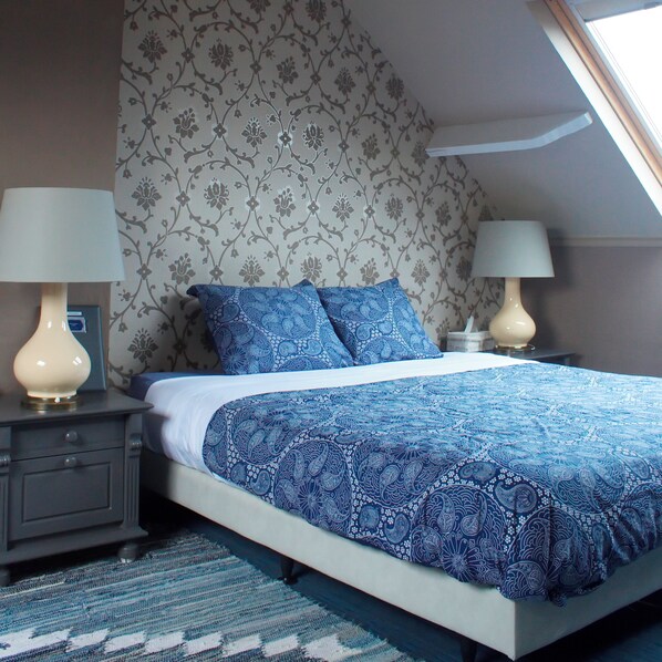 Un dormitorio con cama, dos mesitas de noche, una ventana y papel tapiz estampado.