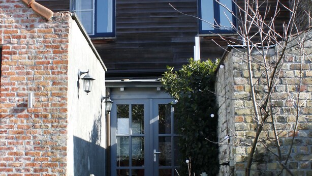 A wooden house with a brick wall, a glass door entrance, and a staircase leading to the front door. - Bed and Breakfast Coupure (Bruges)