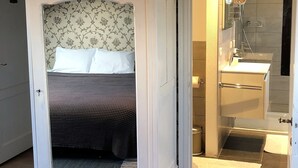 A bedroom with a bed, a white wardrobe, and a bathroom with a shower and sink. - Bed and Breakfast Coupure (Bruges)