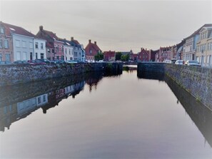 Un canal flanqueado por edificios, un puente de piedra y coches aparcados.
