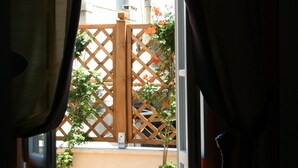 Ein Zimmer mit einem Bett, einem Fenster mit Vorhängen und Blick auf einen Holzzaun und Pflanzen draußen.