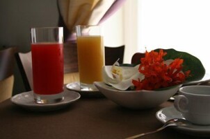 Una mesa con un vaso de jugo de uva, un vaso de jugo de naranja, un cuenco de flores y una taza blanca.