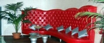 A red sofa with metallic cushions, a glass coffee table, and a potted plant.