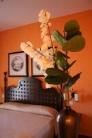 Una cama con cabecera, un florero con planta y un cuadro en la pared.