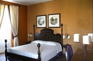 A hotel room with a wooden four-poster bed, two framed pictures on the wall, a desk with a chair, and a lamp.