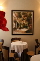 Un área de comedor con una mesa y sillas, un cuadro en la pared y una flor roja en primer plano.