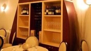 Ein Essbereich mit einer markanten Holzkonstruktion, kreisrunden Ausschnitten, Regalen mit Flaschen und einem runden Tisch mit Stühlen.
