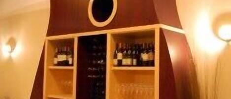 A dining area with a unique wooden structure with circular cutouts, shelves with bottles, and a round table with chairs.
