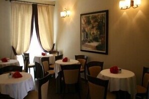 A dining area with round tables, chairs, and a painting on the wall. - Hotel dei Coloniali (Syracuse)