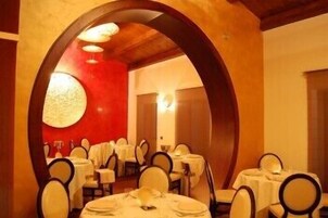 A dining area with round tables and chairs, a red accent wall, and a wooden ceiling.
