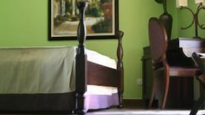 Ein Zimmer mit einem Bett, einem Bild an der Wand, einem Schreibtisch mit Computer und einer Vase mit Blumen.