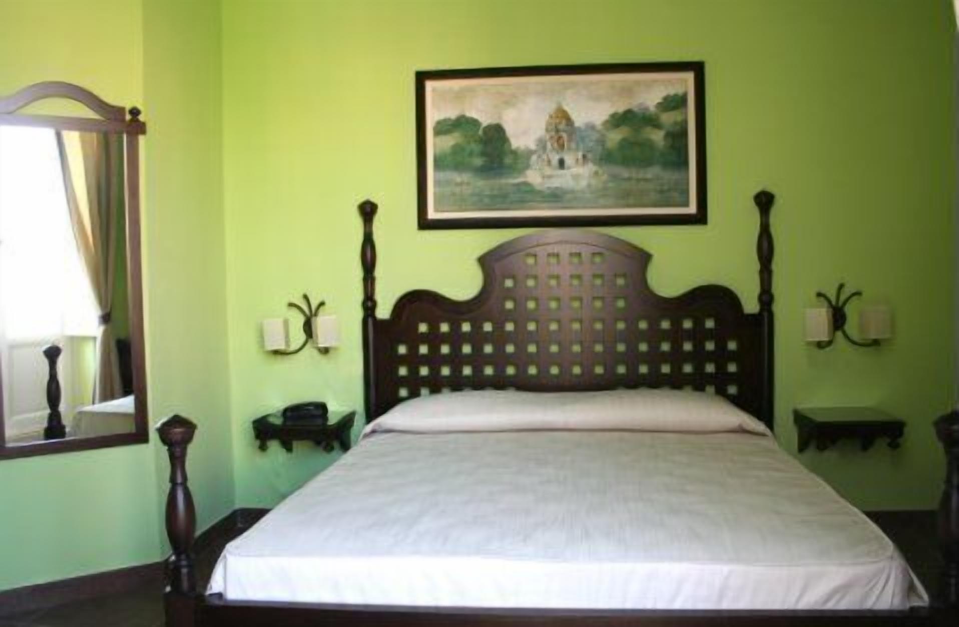 A room with a bed, a painting on the wall, and a window with curtains.
