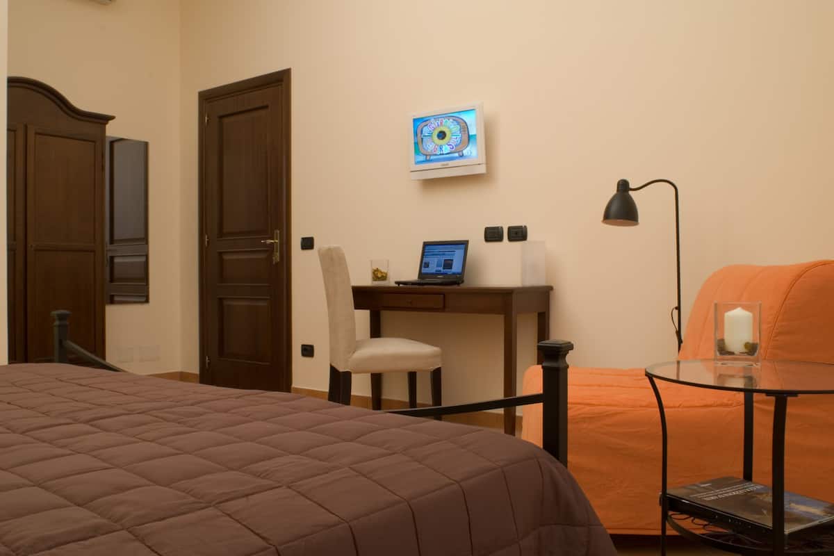 A bedroom with a bed, a desk with a laptop, a chair, a lamp, and a sofa.