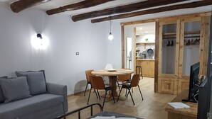 A cozy room with a grey sofa, a round dining table with chairs, a wooden door leading to a kitchen, and a TV on a wooden stand. - Portanova (Naples)
