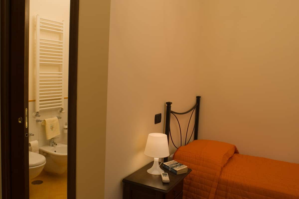 A hotel room with a bed, a nightstand with a lamp, a book, and a remote control.