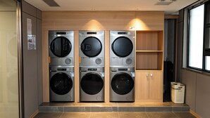 A laundry room with three stacked washing machines, a trash bin, and a wooden cabinet. - Junshan Hotel (Guangzhou)