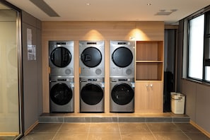 A laundry room with three stacked washing machines, a trash bin, and a wooden cabinet. - Junshan Hotel (Guangzhou)