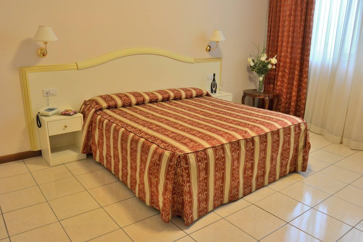 A neatly made bed with a striped bedspread, a bedside table with a lamp, and a vase with flowers on a nightstand.