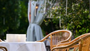 A table with a white tablecloth and a candle, surrounded by wicker chairs in an outdoor setting with greenery in the background. - Tenuta Delo Relais (Verona)