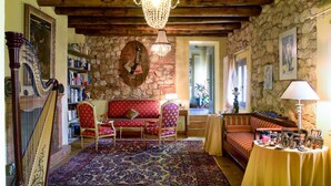 A room with a stone wall, a harp, a red sofa, a patterned rug, and a table with various items. - Tenuta Delo Relais (Verona)