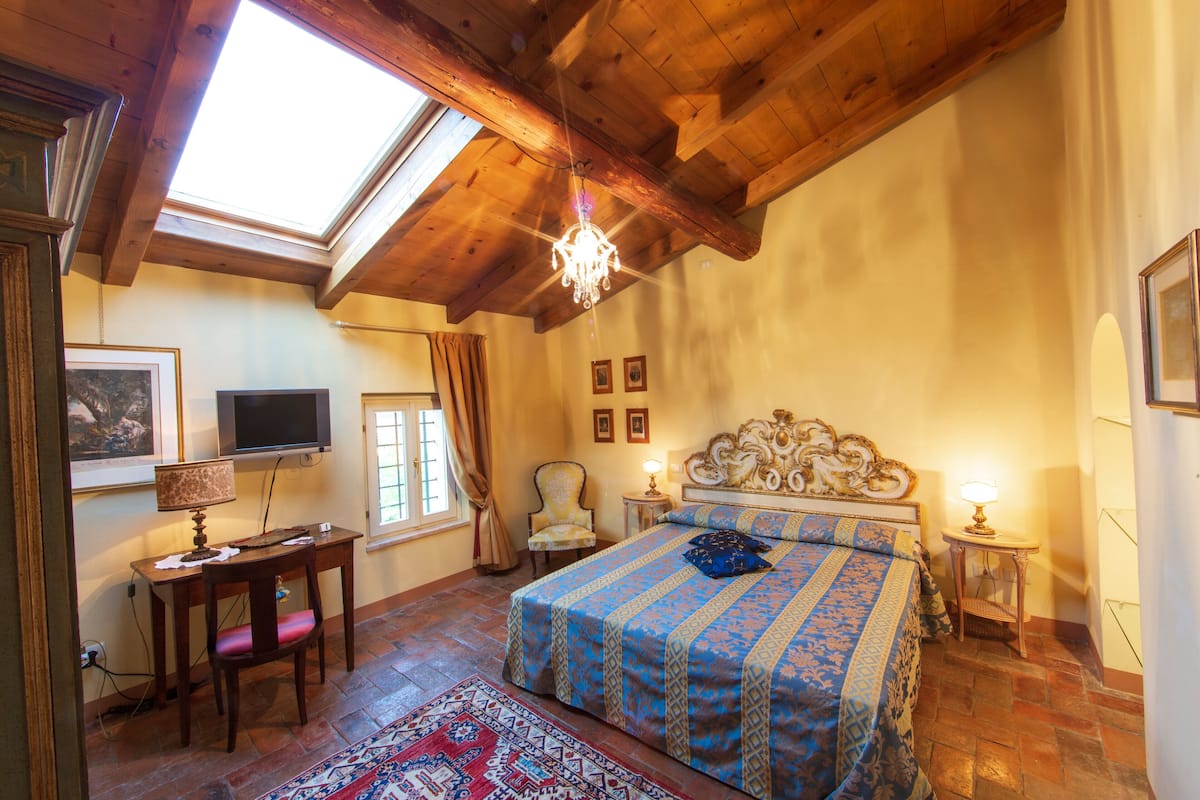 Une chambre à coucher avec un grand lit, un bureau, une chaise, une télévision et un lustre.