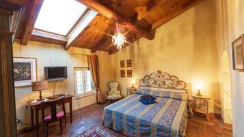A bedroom with a large bed, a desk, a chair, a television, and a chandelier.