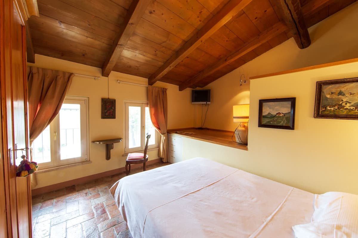 Une chambre avec un plafond en bois, un lit, une chaise, une petite table et un téléviseur fixé au mur.