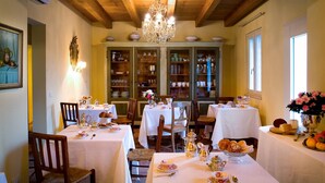 A dining area with wooden beams and a chandelier, featuring tables set for tea service with porcelain and silverware. - Tenuta Delo Relais (Verona)