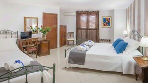 A hotel room with two beds, a desk with a computer, a chair, a TV, a plant, and a painting on the wall. - Garibaldi Relais (Sciacca)