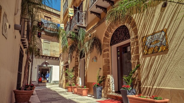 A narrow street with terracotta pots and potted plants lining the sidewalk. - Garibaldi Relais (Sciacca)