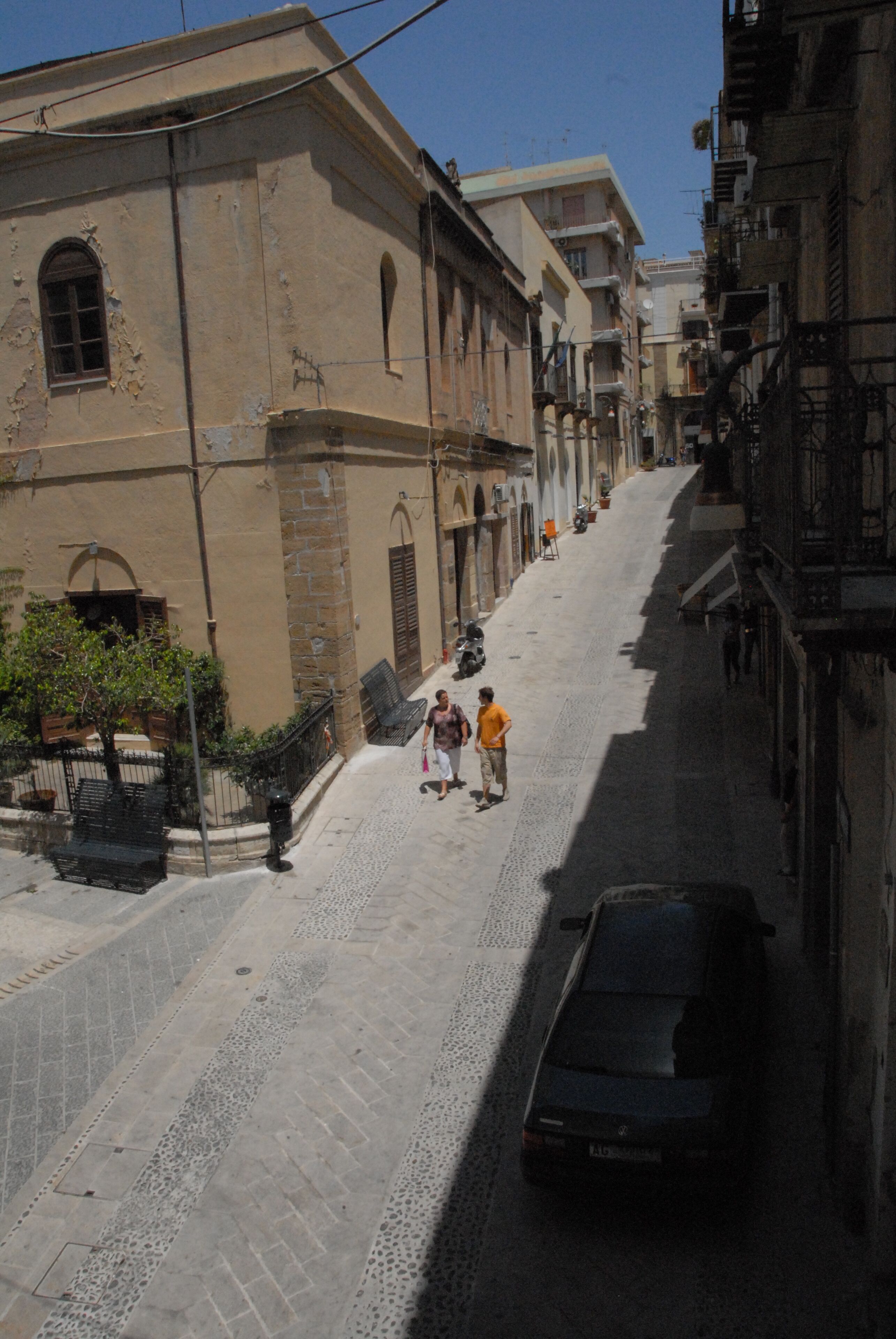 A narrow cobblestone street lined with historic buildings, a parked car, and a few pedestrians.