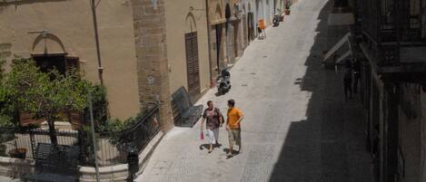 A narrow cobblestone street lined with historic buildings, a parked car, and a few pedestrians.