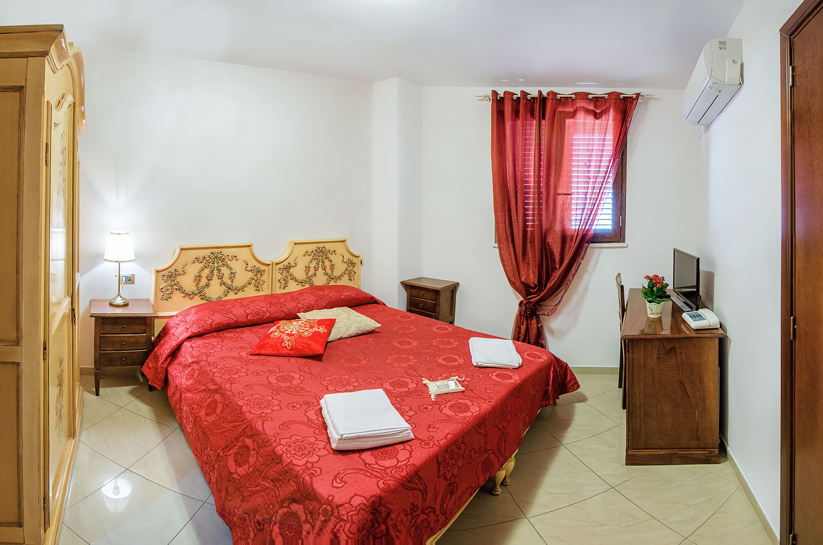 A bedroom with a large bed, a bedside table with a lamp, a dresser, and a window with curtains.