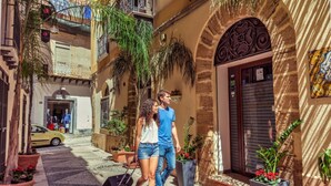 A narrow street with a building entrance, potted plants, and a red carpet. - Garibaldi Relais (Sciacca)