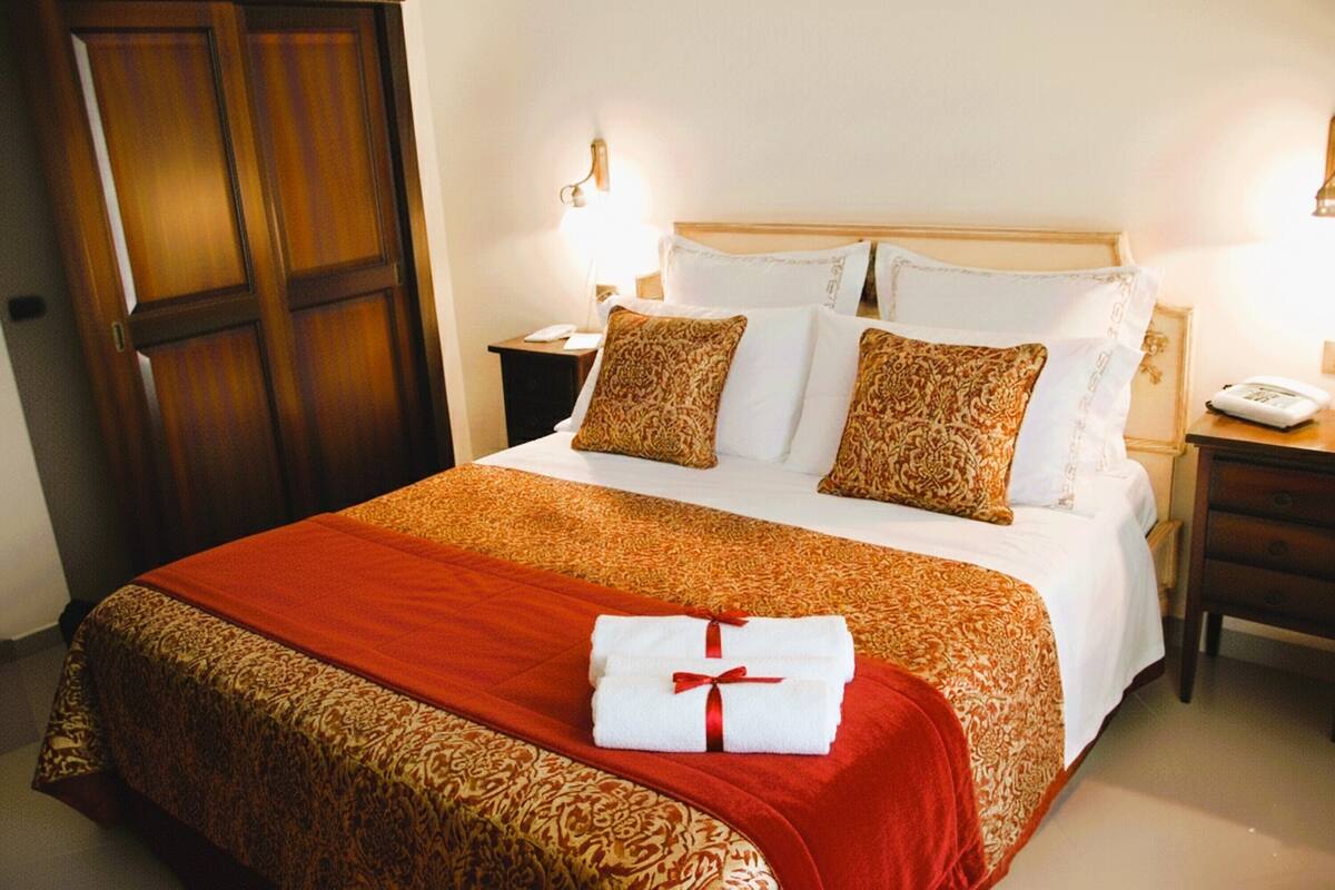 A hotel room with a large bed, a wooden wardrobe, a bedside table with a lamp, and a telephone.