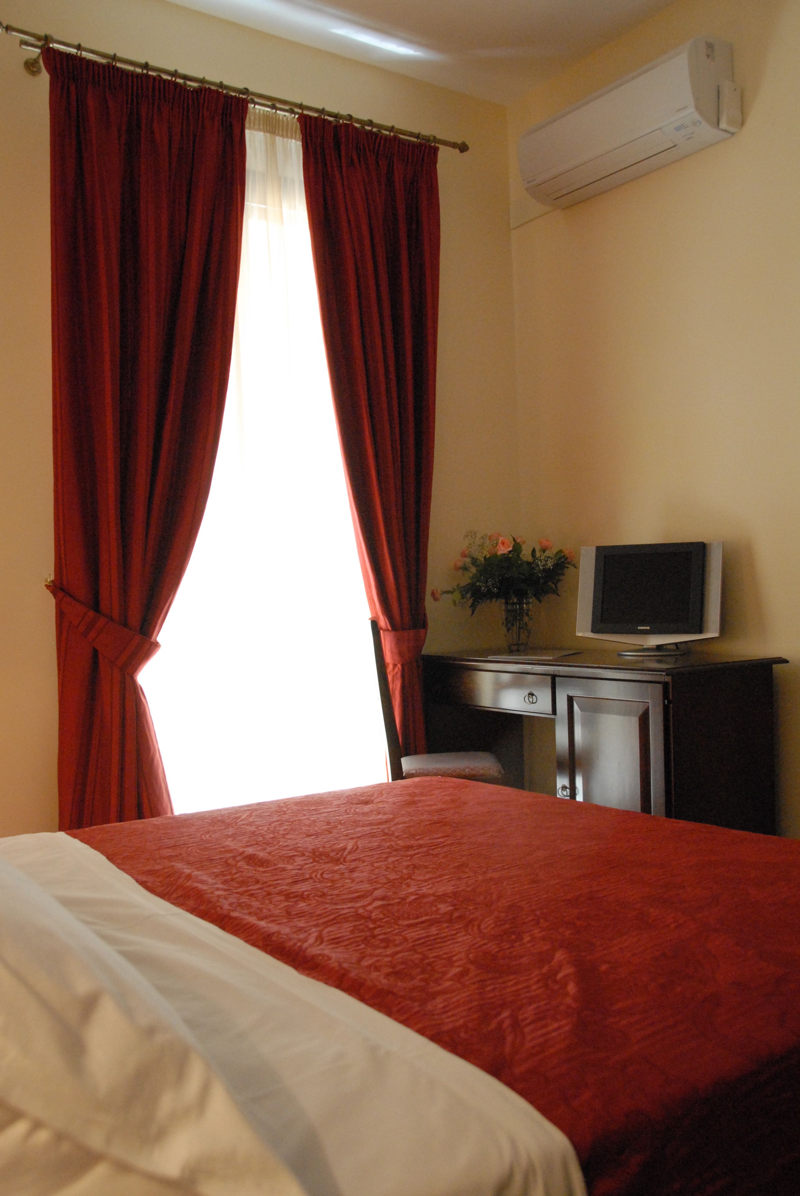 A hotel room with a bed, a desk, a television, and an air conditioning unit.