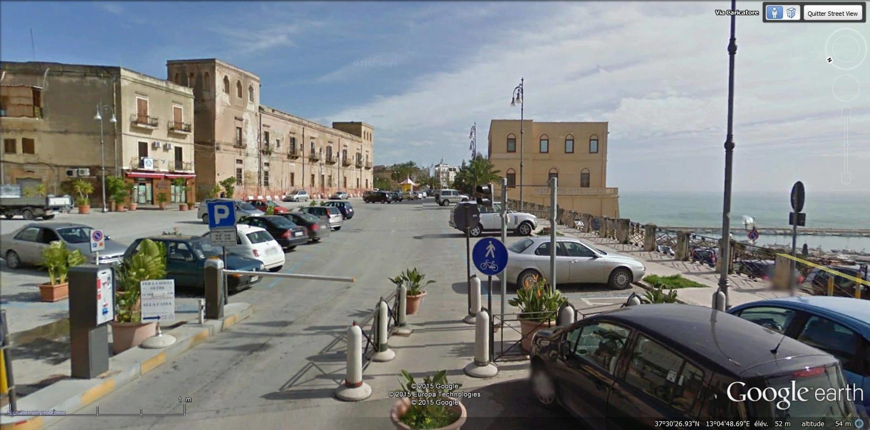 Vista de una calle con autos estacionados, un paso de peatones y edificios con balcones.