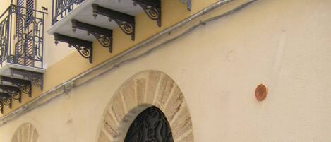 Ein Gebäude mit Rundbogenportalen, einem Wappen auf dem Schild und Blumentöpfen am Eingang.
